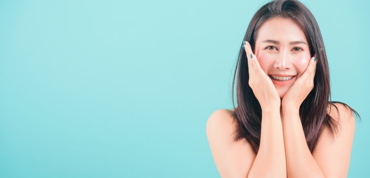 Asian happy portrait beautiful young woman standing smiling surprised excited her hands over her face and looking to camera on blue background with banner copy space for text