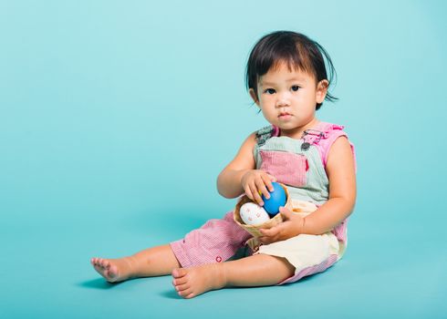 Asian Cute little baby girl beautiful holding Easter egg in basket, studio shot on blue background with copy space, Easter day concept