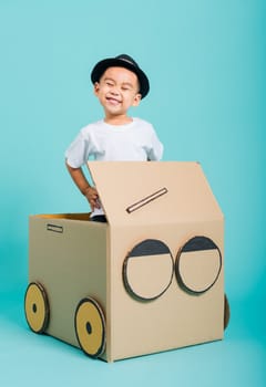 Happy Asian children boy smile in driving play car creative by a cardboard box imagination, summer holiday travel concept, studio shot on blue background with copy space for text