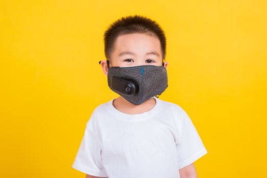Asian Thai happy portrait cute little cheerful child boy wearing mask protective for covid-19 or pm2.5 dust he looking to camera, studio shot isolated on yellow background with copy space
