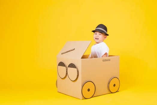 Portrait happy Asian cute little children boy smile so happy wearing white T-shirt driving car creative by cardboard, studio shot on yellow background with copy space