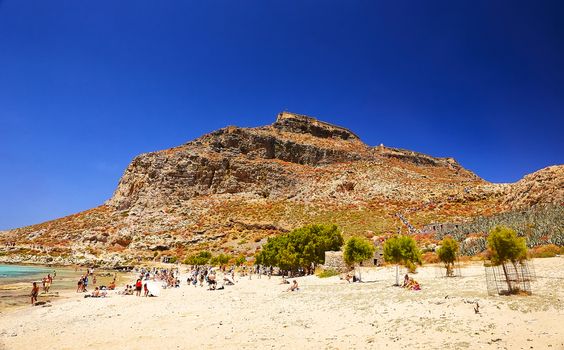 GRAMVOUSA - BALOS, THE CRETE ISLAND, GREECE - JUNE 4, 2019: The people are on the beach near the pirate castle mountain.