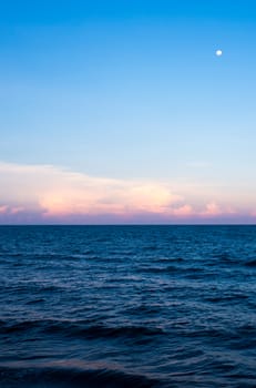 Pink Clouds and moon in sunset sky over sea