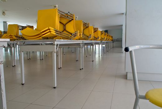 Many yellow plastic chairs stacked on the table