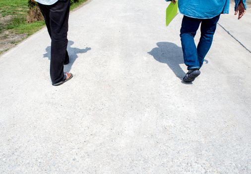 The legs of two men are walking together on concrete walkway