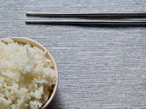 Rice in a cup and metal chopsticks on gray background