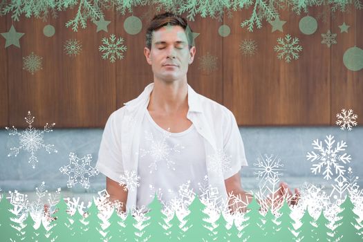 Handsome man in white meditating in lotus pose against snowflakes and fir trees in green