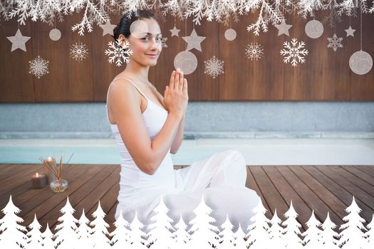 Content brunette in white sitting in lotus pose smiling at camera against fir tree forest and snowflakes