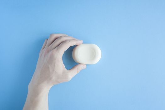 A piece of soap in a male hand a top view on a blue background. The human hand holds soap. Wash your hands. Soap against bacteria and viruses. Compliance with hygiene and sterility to combat coronavirus.