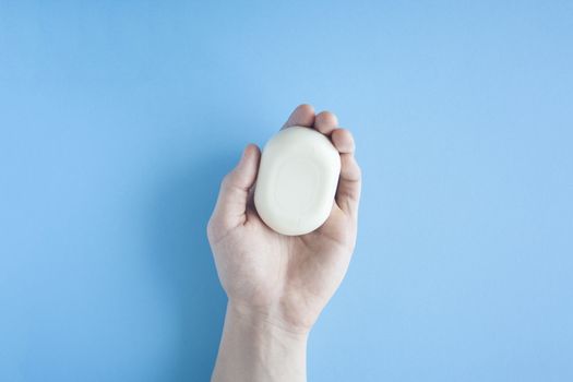 A piece of soap in a male hand a top view on a blue background. The human hand holds soap. Wash your hands. Soap against bacteria and viruses. Compliance with hygiene and sterility to combat coronavirus.