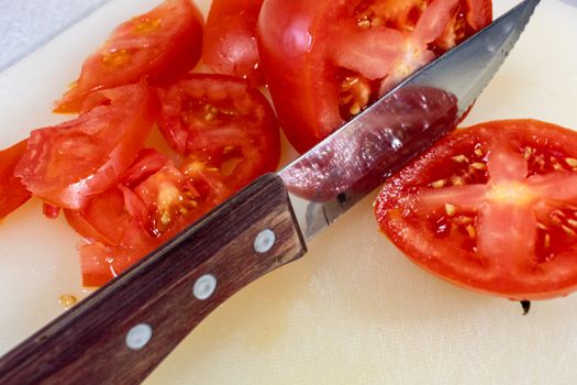 A steak knife with a wooden handle slices through a red beefsteak tomato on a cutting board.