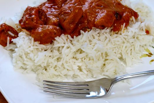 A vegetarian dish of broccoli and simulated chicken is served up with a butter chicken tomato sauce from Indian cuisine on a bed of basmati rice. It is seen from a high angle with a metal fork on a plate.
