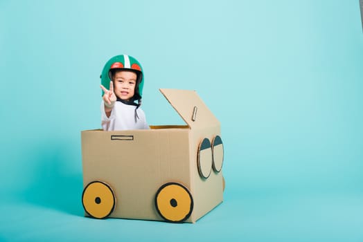 Happy Asian children boy with Helmet smile in driving play car creative by a cardboard box imagination, summer holiday travel concept, studio shot on blue background with copy space for text