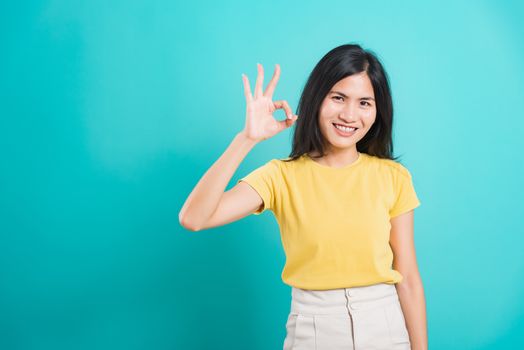 Portrait Asian beautiful young woman standing, She made finger OK symbol sign to agree and looking at camera, shoot photo in studio on blue background, There was copy space