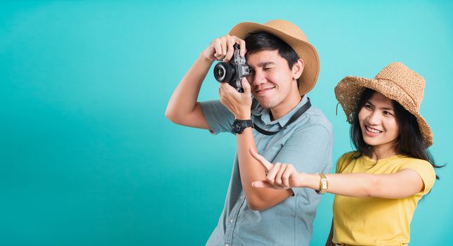 Happy Asian excited couple young beautiful woman point finger and handsome man holding camera shot photography in summer holiday travel tourists isolated on blue background with copy space for text