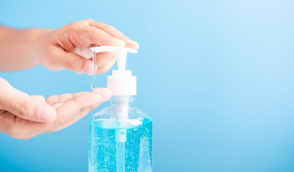 Close up Asian young woman applying press dispenser sanitizer alcohol gel pump to hand wash cleaning, hygiene prevention COVID-19 or coronavirus protection concept, isolated on blue background