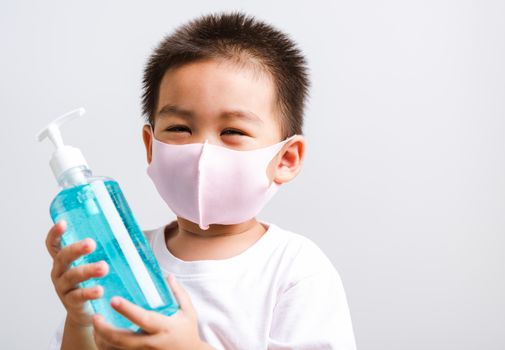 Closeup portrait Asian little child boy holding show bottle pump dispenser sanitizer alcohol gel hand wash cleaning, COVID-19 or coronavirus protection concept, isolated on white background