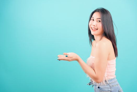 Smiling face Asian beautiful woman her showing holding something with two hands and looking to camera on blue background, with copy space for text