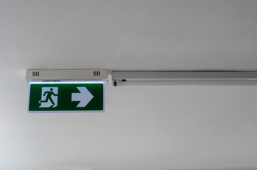 Exit signs, fire exits and arrows pointing the way on the light signs on the ceiling of corridors in the building.