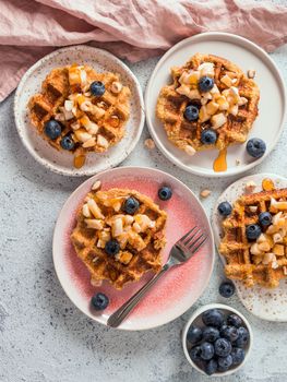 Easy healthy gluten free oat waffles with copy space. Plates with appetizing homemade waffles with oat flour decorated blueberries, bananas and honey on gray background. Vertical. Top view or flat lay