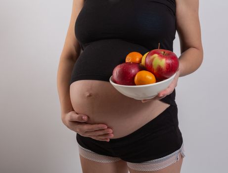 Pregnancy and healthy organic nutrition. Pregnant woman holds fresh vitamin fruits, free space. Place for text. Concept of expectation and health