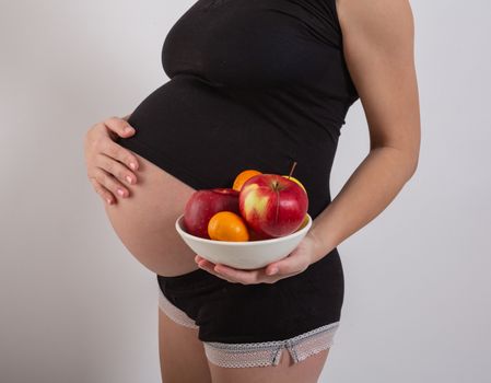 Pregnancy and healthy organic nutrition. Pregnant woman holds fresh vitamin fruits, free space. Place for text. Concept of expectation and health