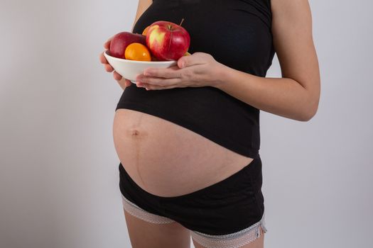 Pregnancy and healthy organic nutrition. Pregnant woman holds fresh vitamin fruits, free space. Place for text. Concept of expectation and health