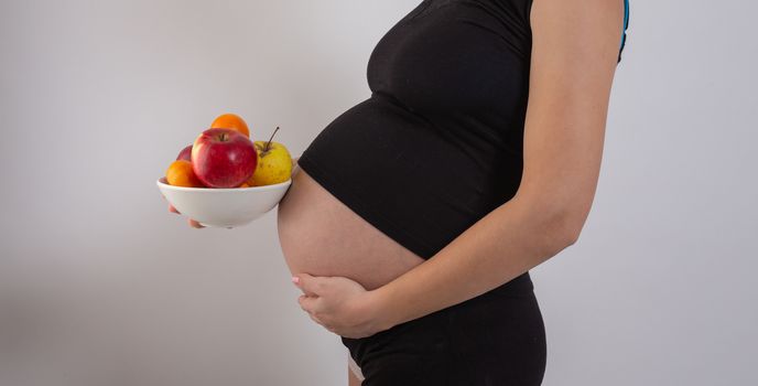 Pregnancy and healthy organic nutrition. Pregnant woman holds fresh vitamin fruits, free space. Place for text. Concept of expectation and health