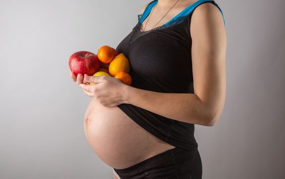 Pregnancy and healthy organic nutrition. Pregnant woman holds fresh vitamin fruits, free space. Place for text. Concept of expectation and health