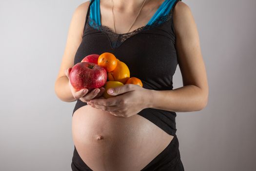 Pregnancy and healthy organic nutrition. Pregnant woman holds fresh vitamin fruits, free space. Place for text. Concept of expectation and health