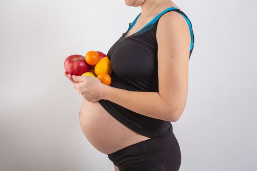 Pregnancy and healthy organic nutrition. Pregnant woman holds fresh vitamin fruits, free space. Place for text. Concept of expectation and health