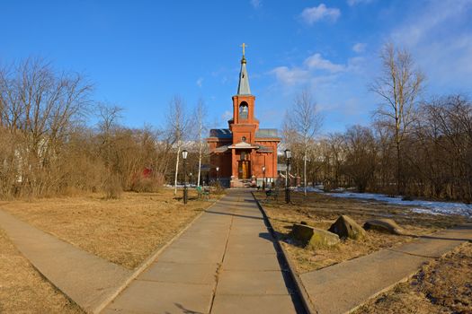 The Orthodox church of red brick surrounded by trees under a blue sky lit by the evening light of the sun in spring.