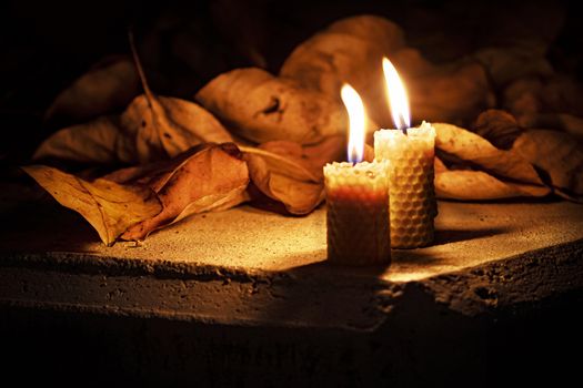 background Two beeswax candles on concrete with dry leaves