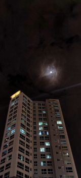Moon shining brightly in the sky with one multistory residential building at night in Korea