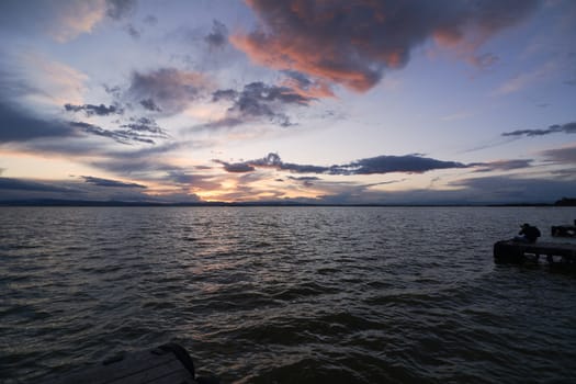 Landscape of a lake with storm clouds, moving waters reeds in the water, bluish tones, pier