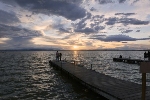 Landscape of a lake with storm clouds, moving waters reeds in the water, bluish tones, pier,