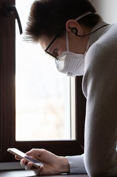 A young man in a reusable medical mask looks at the phone screen for information on how to protect yourself from the coronavirus