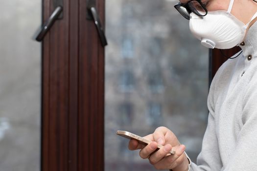 A young man in a reusable medical mask looks at the phone screen for information on how to protect yourself from the coronavirus