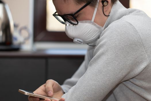 A young man in a reusable medical mask looks at the phone screen for information on how to protect yourself from the coronavirus