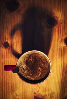 a red cup of coffee with a shadow on a wooden board
