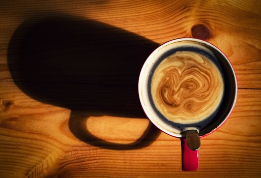 a red cup of coffee with a shadow on a wooden board