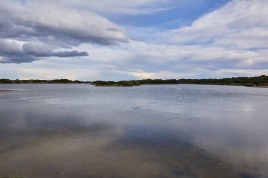 Lake with calm waters after the storm, dramatic clouds, blue sky and reflections in the water