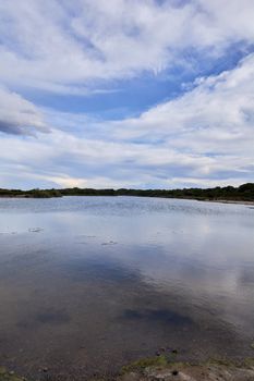 Lake with calm waters after the storm, dramatic clouds, blue sky and reflections in the water