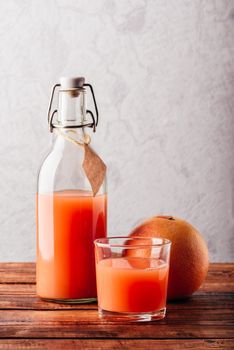 Bottle of grapefruit juice with glass and fruit on wooden surface