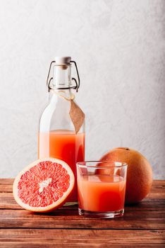 Bottle of grapefruit juice with glass and fruit on wooden surface