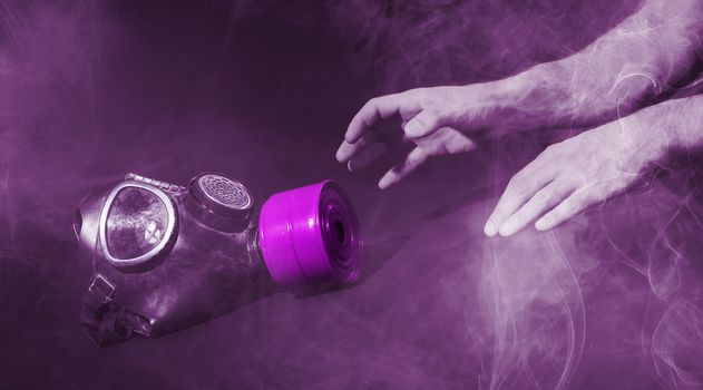 Man in room filled with smoke, trying to reach for vintage gasmask - Isolated on black - Purple smoke
