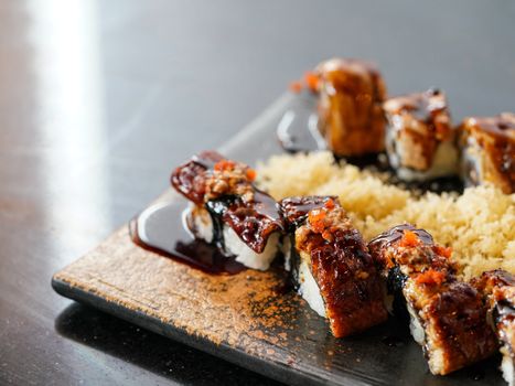 Anago sushi topped with Foie Gras, served with tempura crust on a black plate. Japanese Cuisine Buffet.