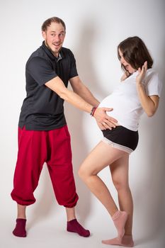 Handsome man is listening to his beautiful pregnant wife's tummy and smiling.