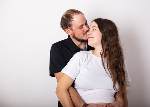 Handsome man is listening to his beautiful pregnant wife's tummy and smiling.