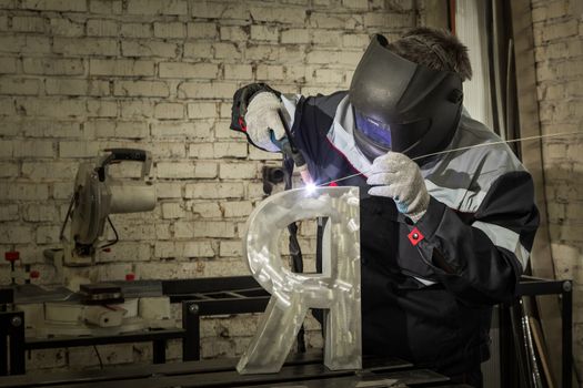 Welder welding a metal part in an industrial environment, wearing standard protection equipment. Sparks flying, fumes, industrial background